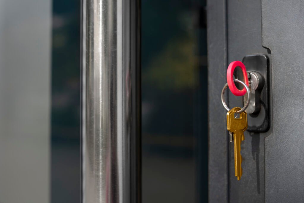 Golden key inserted in door lock with red key ring on gray metal door, representing home ownership, security, and new property access.